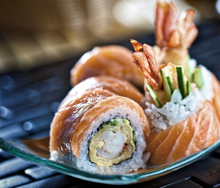 Frischer Lachs-Tempura-Maki mit Garnelen und Gurken auf einer eleganten Sushi-Platte.